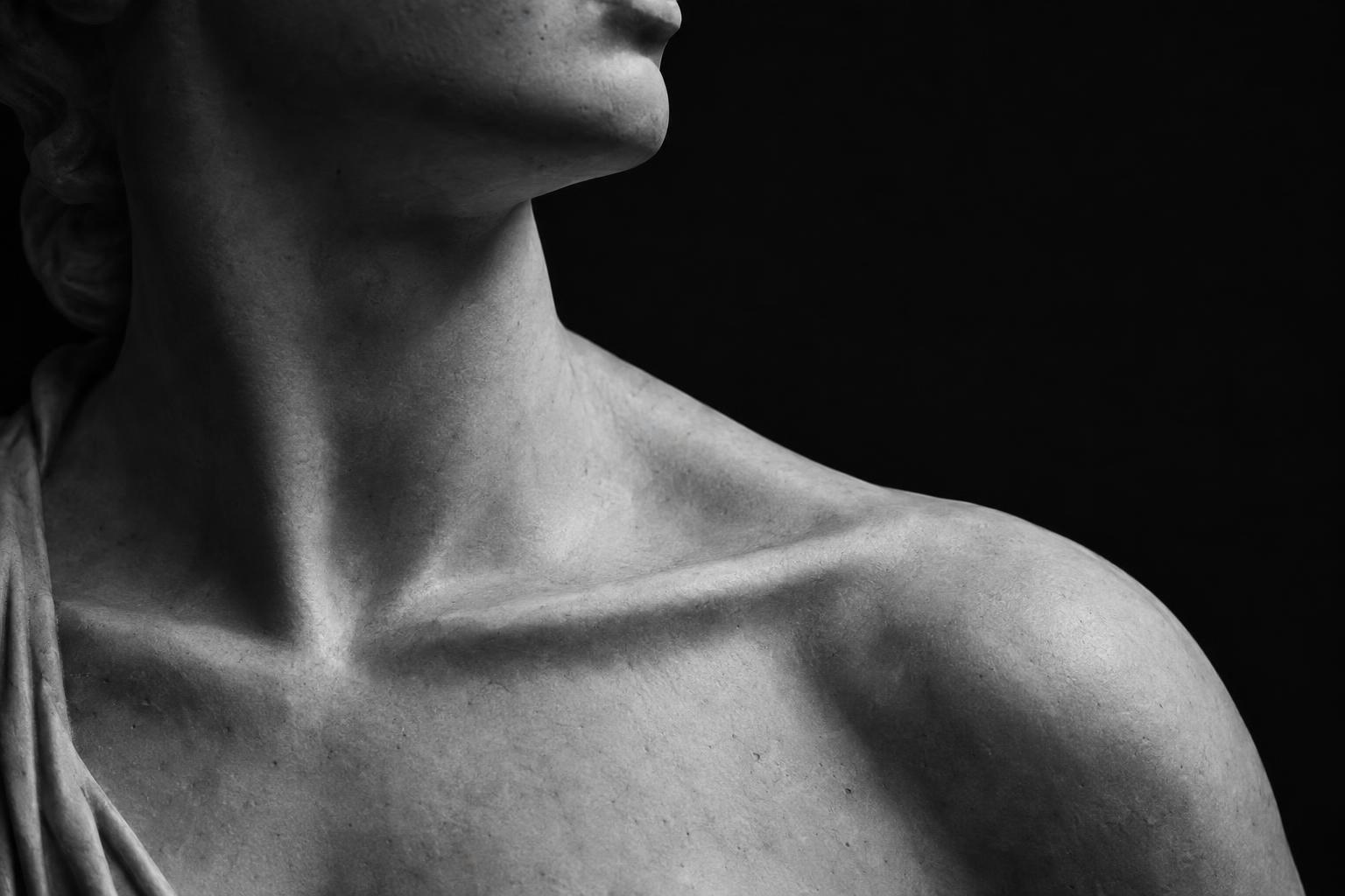 Close crop of a classical marble statue's neck, jawline and collarbone in dramatic light